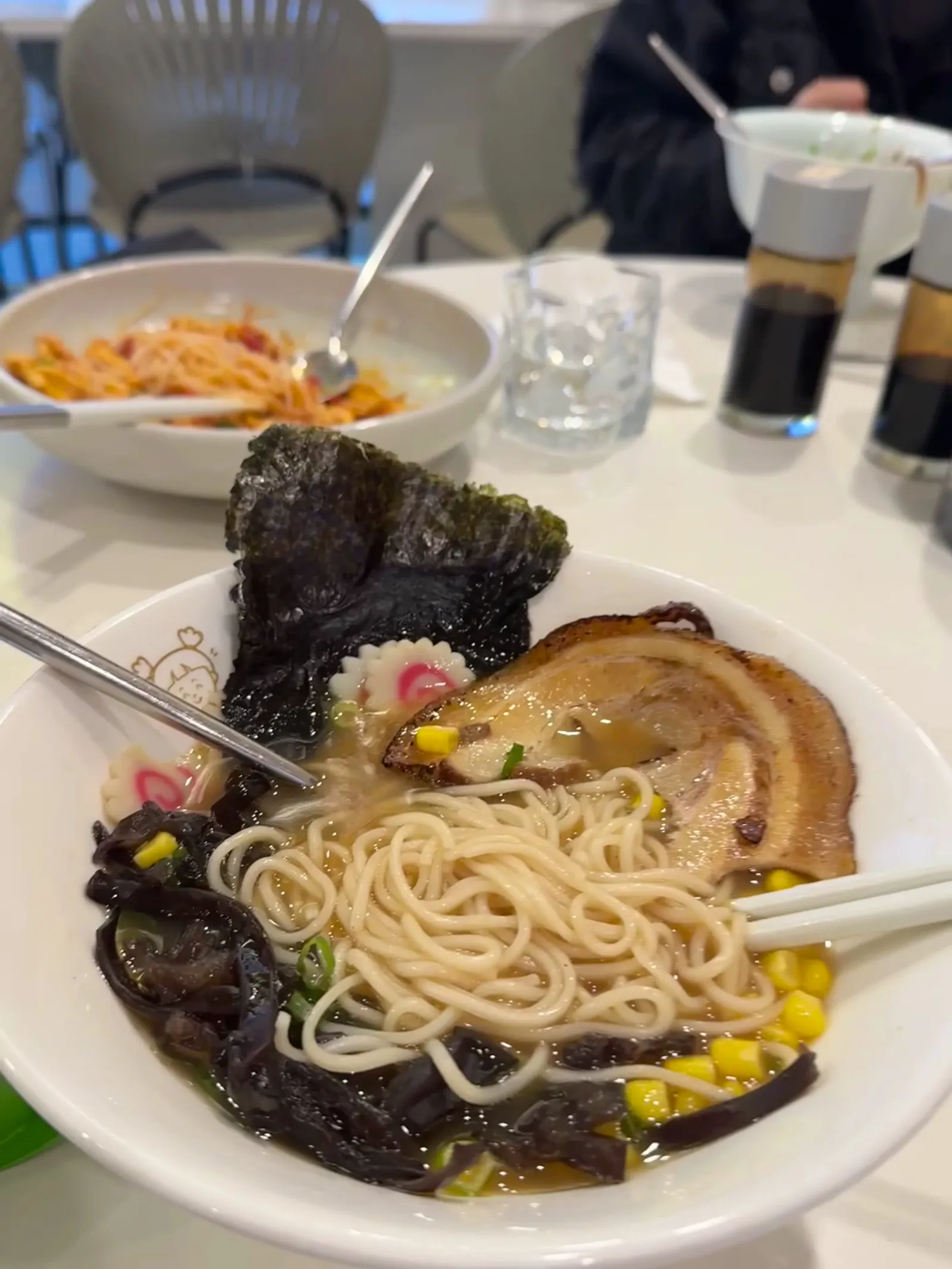 White bowl of black garlic ramen with chashu pork, nori, corn and narutomaki fish cakes