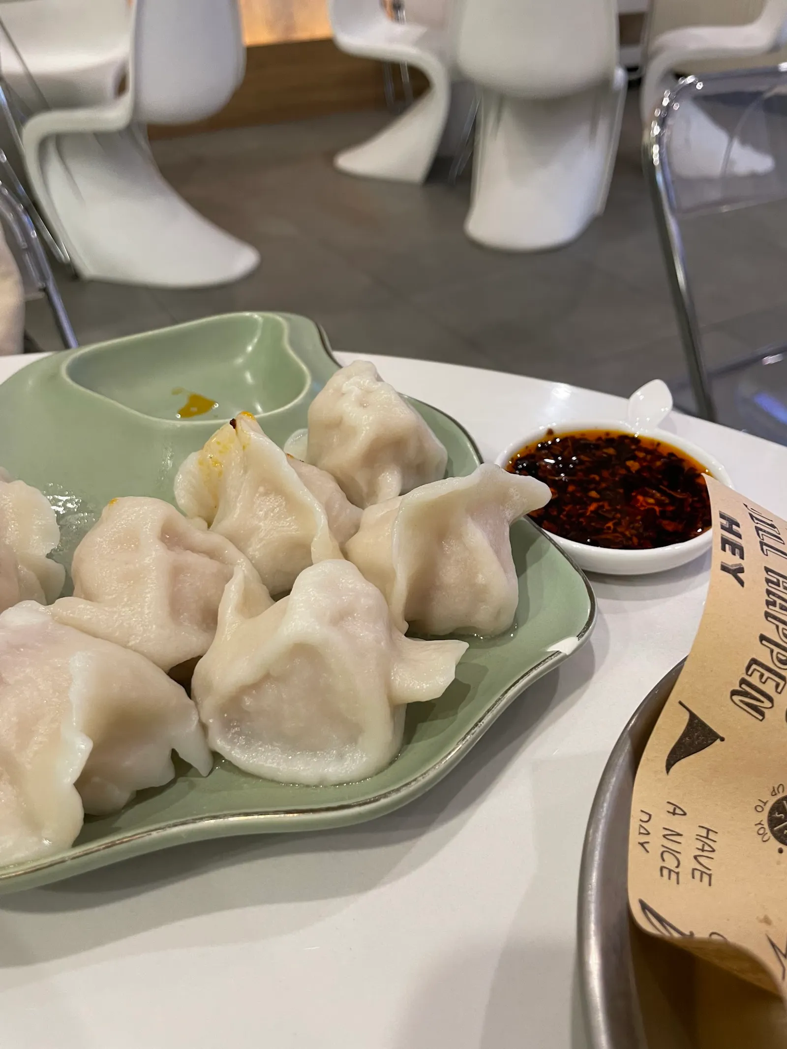 Steamed dumplings on celadon plate with chilli oil dipping sauce, white dining room in background