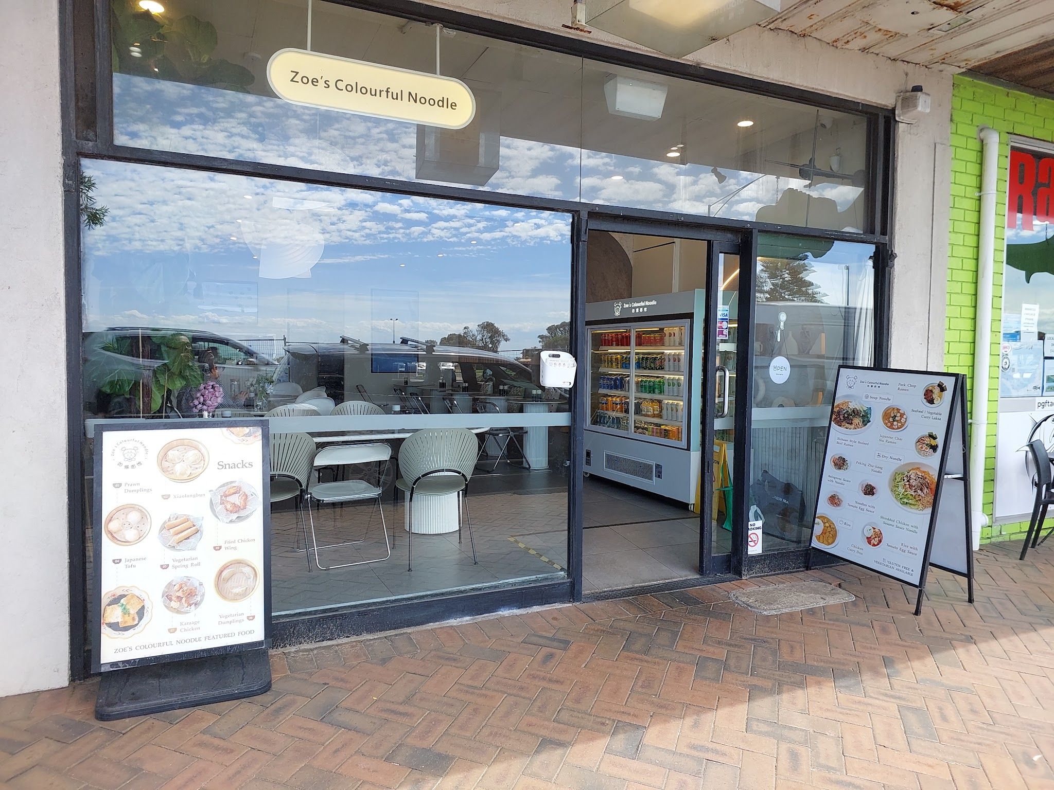 Street-level view of Zoe's Colourful Noodle entrance with A-frame menu boards on footpath
