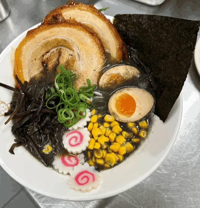 Overhead view of black garlic ramen bowl with chashu pork, soft-boiled egg, nori and corn